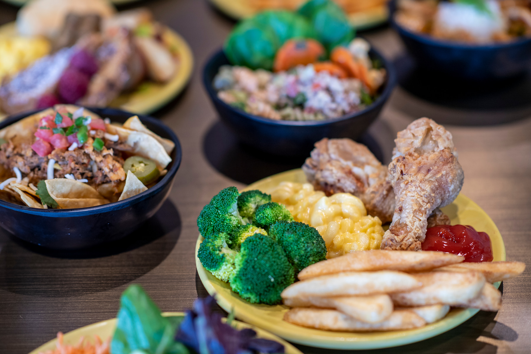 Plates and Bowls filled with food like chicken, fries, broccoli, and nachos