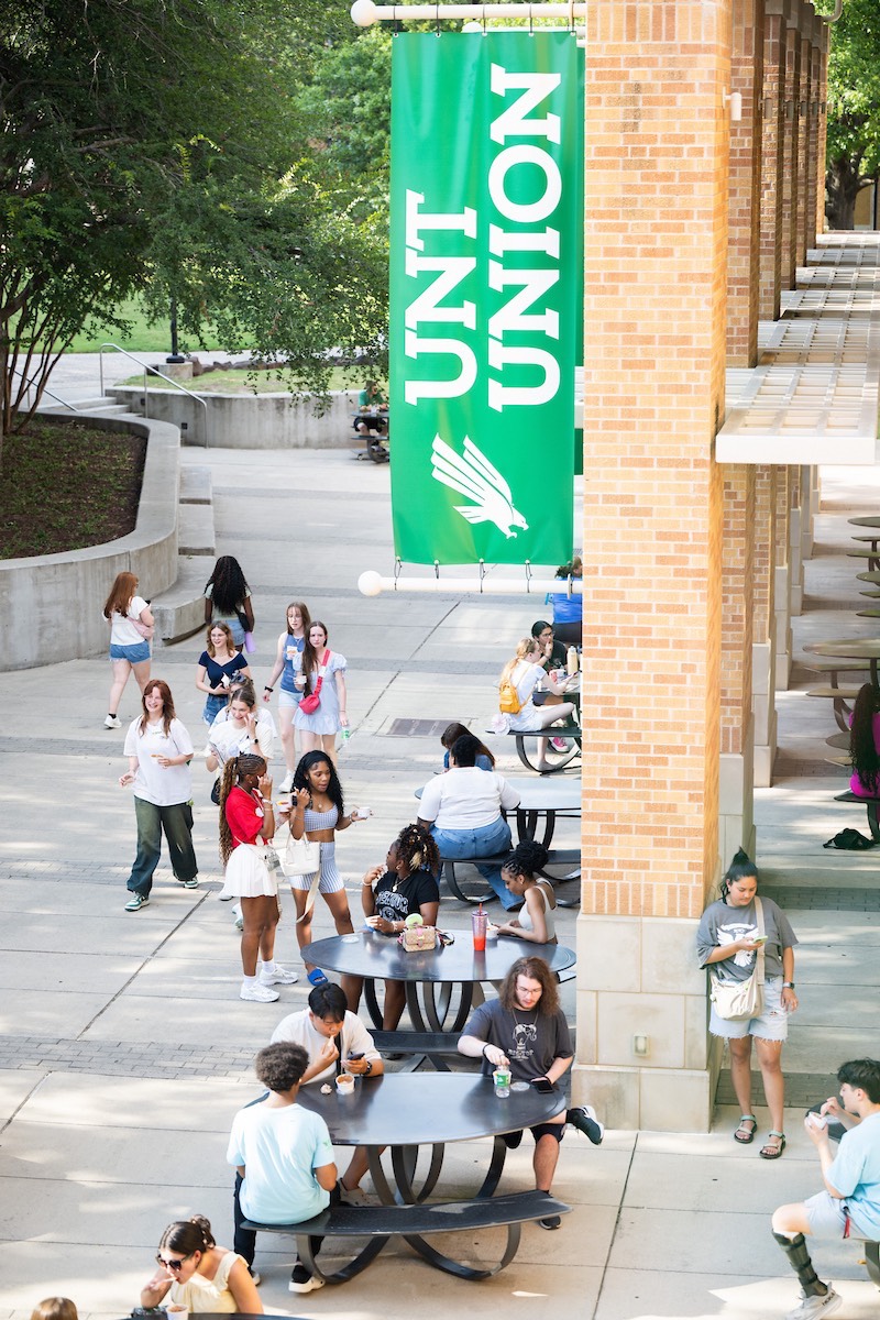 Visitors eating in groups outside the UNT Union, with a banner that reads "UNT Union" hanging from the building