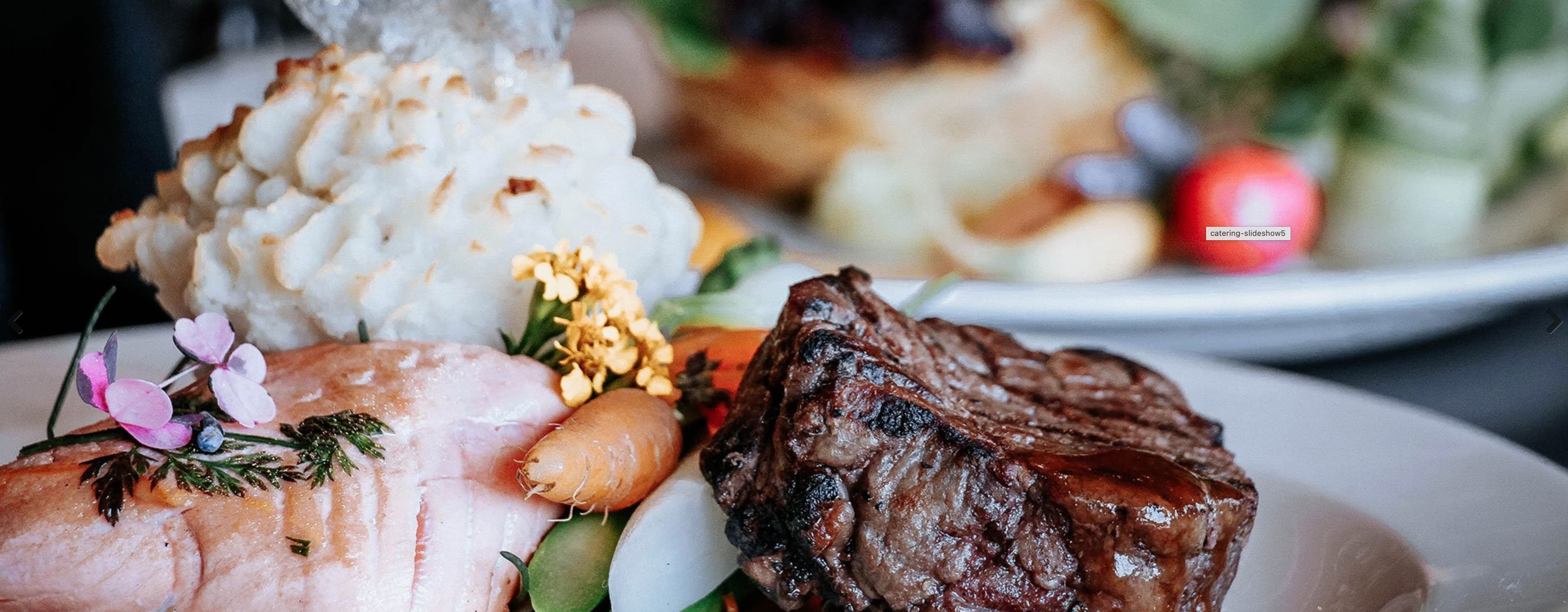 Food prepared on a plate including grilled steak and salmon with potatoes and seasonal vegetables 